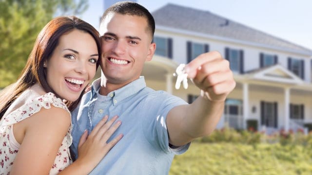 Beautiful young couple holding house keys in front of a new home during a house purchase or real estate transaction.